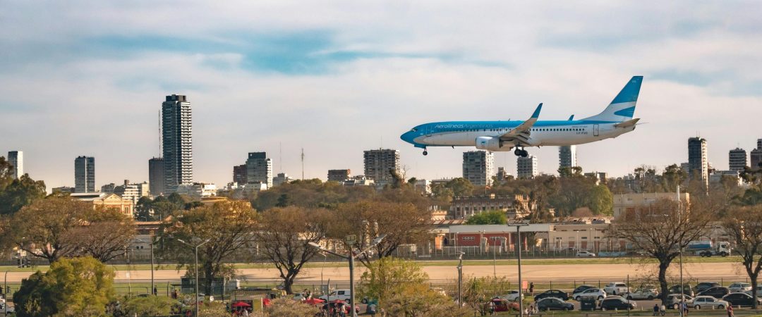 A commercial airplane flies over Buenos Aires' urban park with a city skyline backdrop.